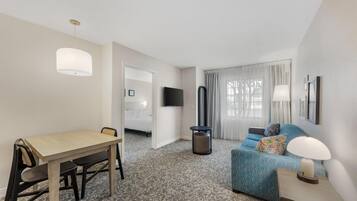 Habitación de hotel con una mesa de comedor, un sofá, un televisor y una lámpara.