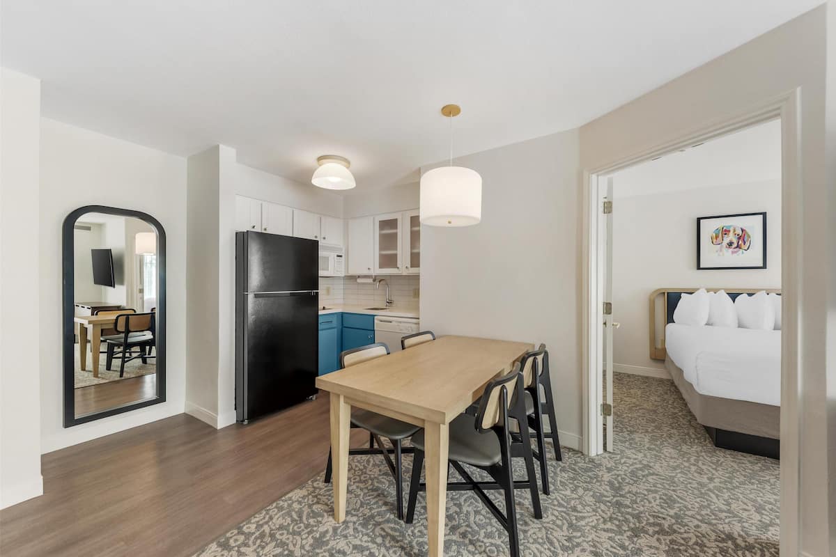 A compact hotel room with a kitchenette, a dining area, and a bed.