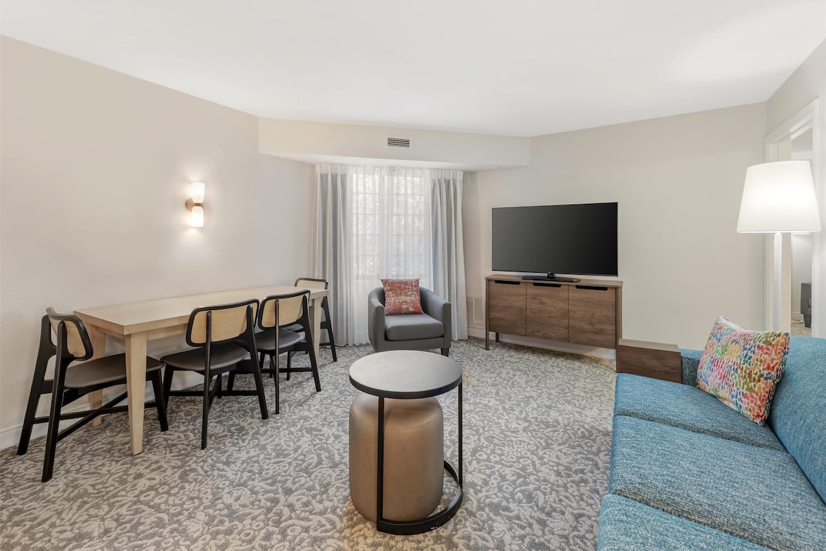 A hotel room with a dining area, a sofa, a TV, and a lamp.