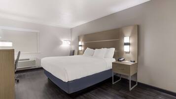 A modern hotel room with a large bed, bedside tables, a desk, and a desk lamp.