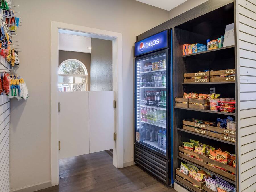 Un corridoio con un frigorifero Pepsi pieno di bevande e snack, una porta che conduce a un'altra stanza e una parete con borse e scatole appese.
