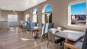 Un espace repas moderne avec des tables et des chaises hautes, de grandes fenêtres et une vue sur l’extérieur.