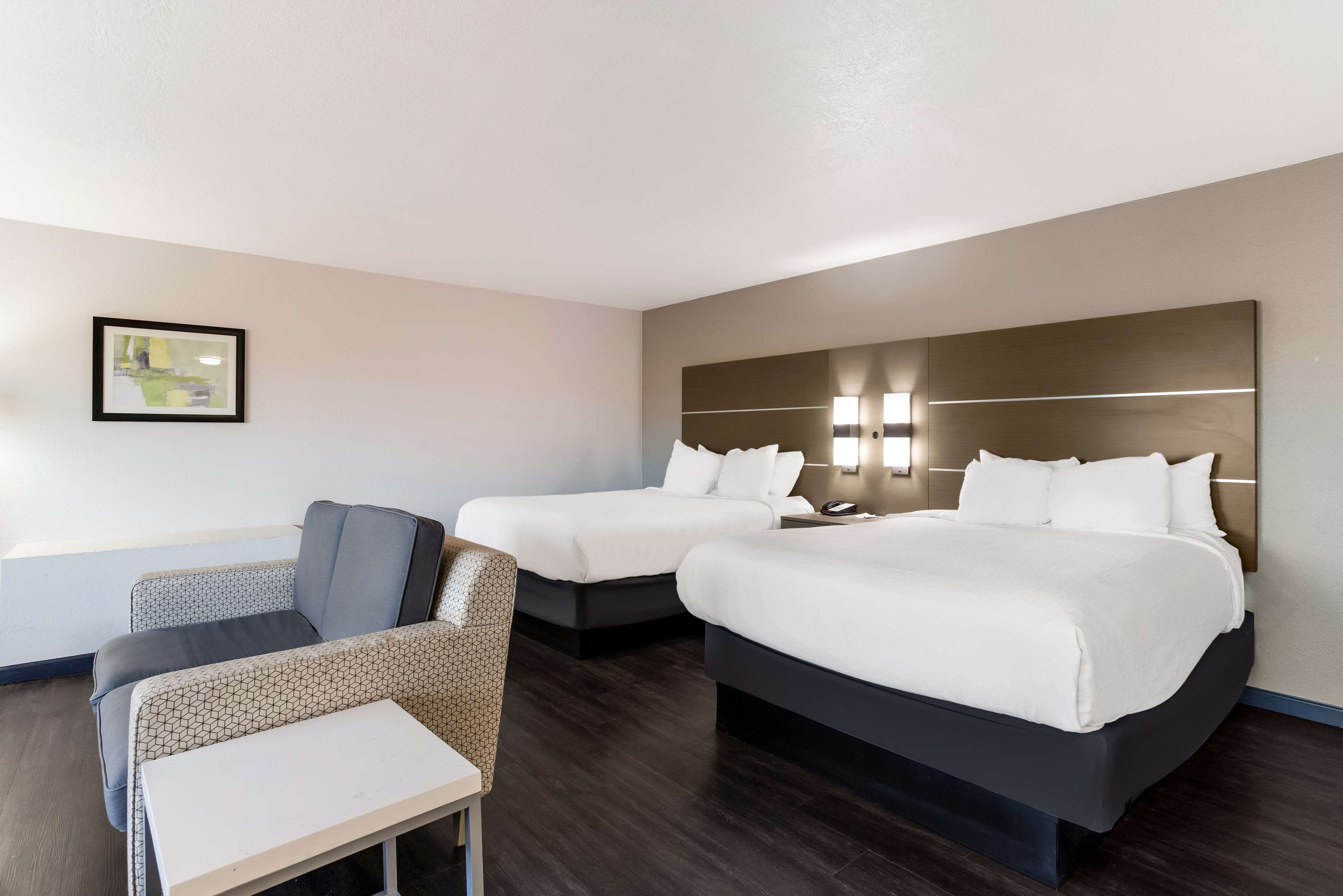 A hotel room with two beds, a small table, and a chair.