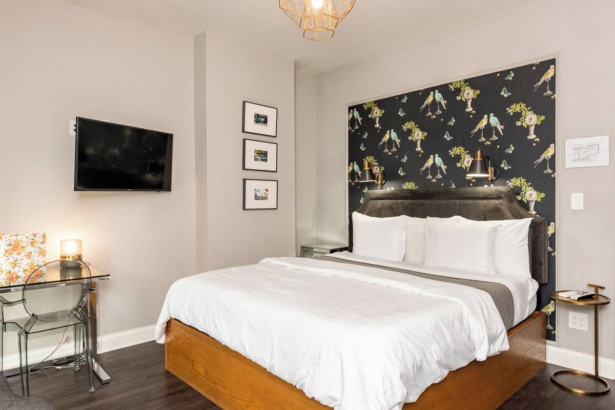 A modern bedroom with a large bed, a glass table, a TV, and a unique bird-patterned headboard.