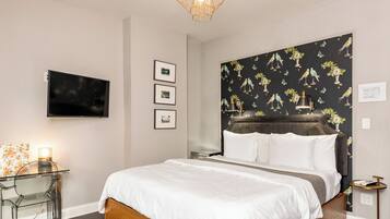 Un dormitorio moderno con una cama grande, una mesa de vidrio, un televisor y un cabecero con estampado de pájaros.