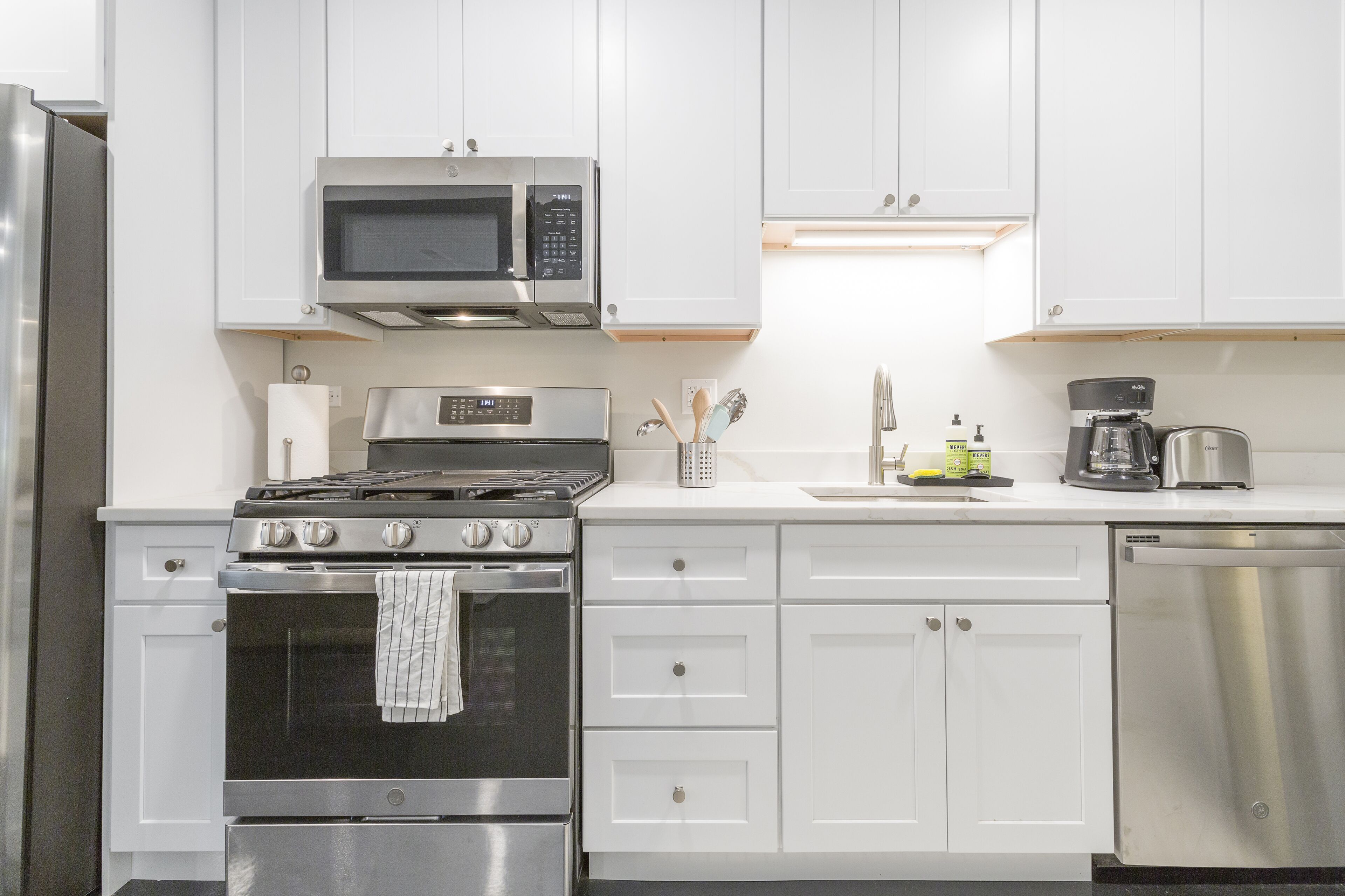 A modern kitchen with white cabinets, stainless steel appliances including a microwave, stove, and dishwasher, and a coffee maker on the counter.