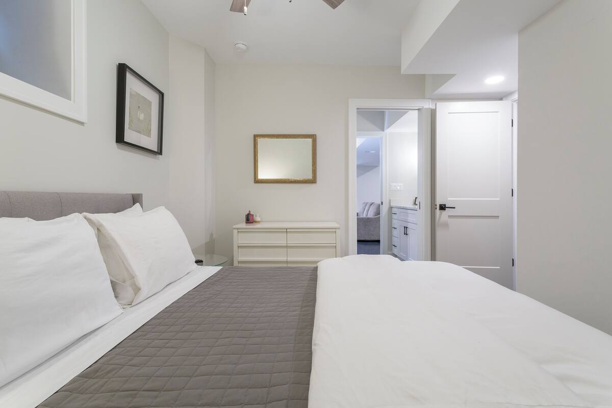A bedroom with a bed, a dresser, a mirror, and a door leading to a bathroom.