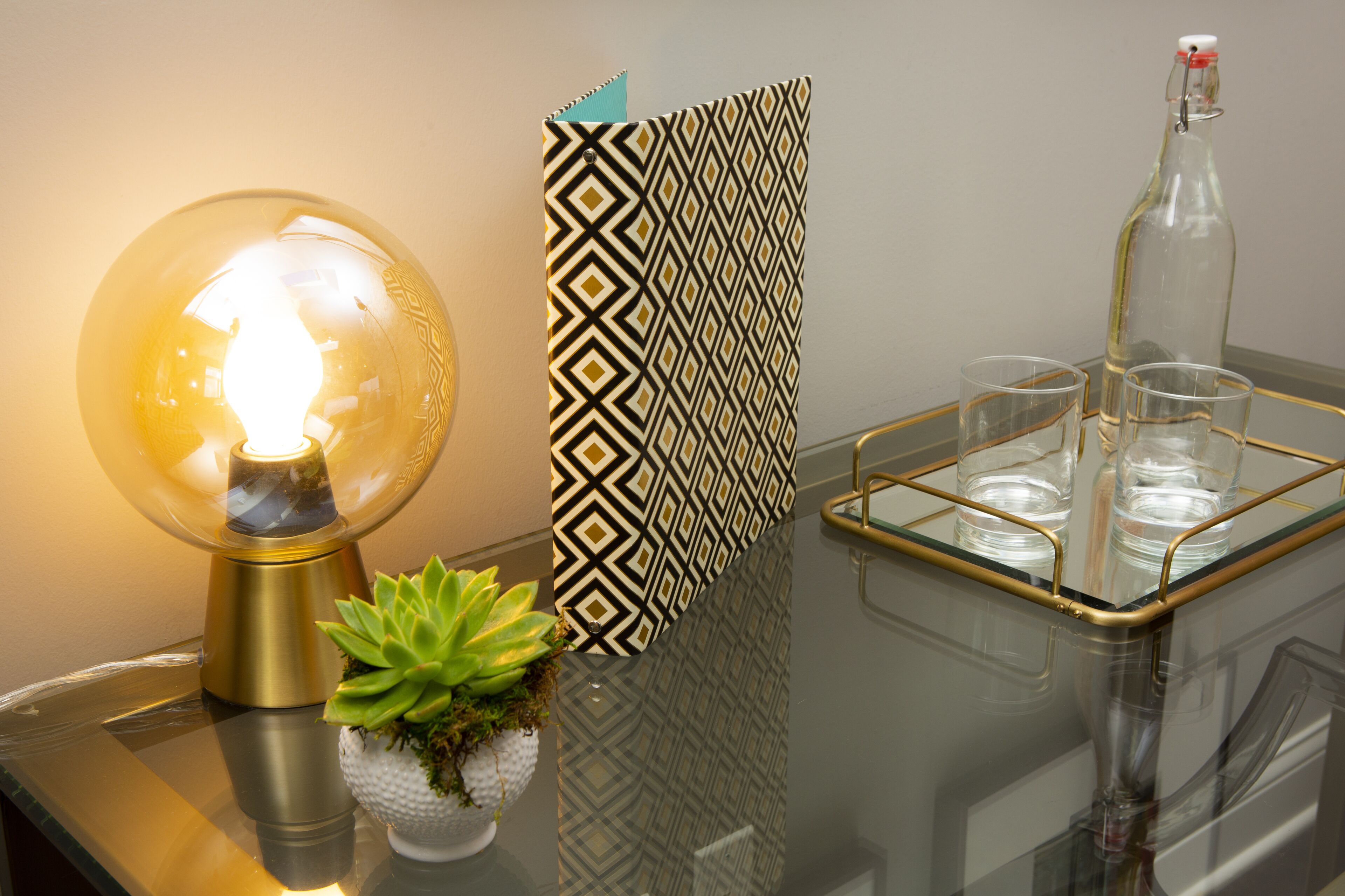 A table with a glass lamp, a patterned card, a glass bottle, and two glasses.