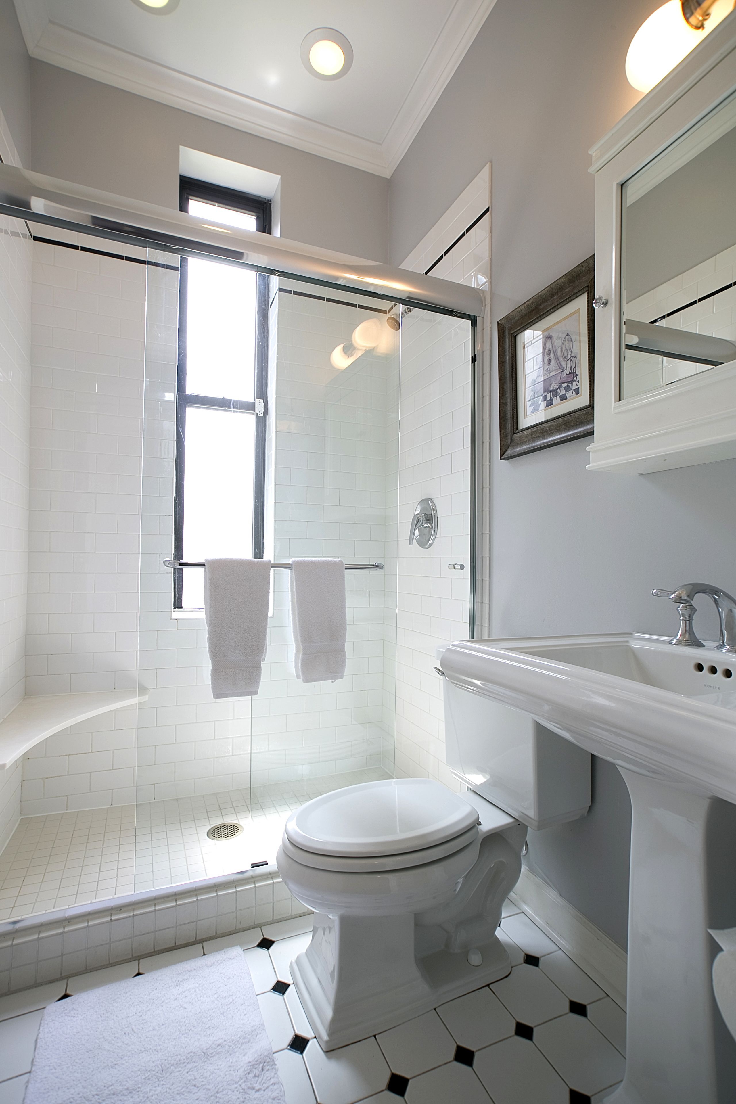 A modern bathroom with a glass-enclosed shower, a white toilet, and a sink with a mirror above it.
