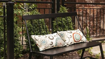 A black metal bench with patterned cushions in front of a brick building with arched windows.