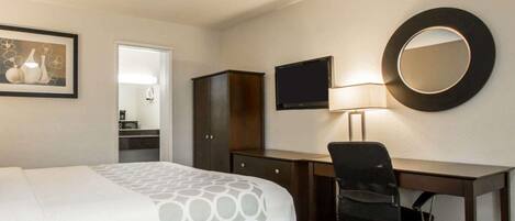 A hotel room with a bed, a desk, a chair, a television, a mirror, and a framed picture on the wall.