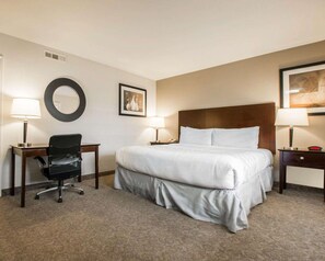 A hotel room with a large bed, two bedside tables, a desk with a chair, a round mirror, and two wall-mounted lamps. - Rodeway Inn Los Angeles Convention Center (Los Angeles)