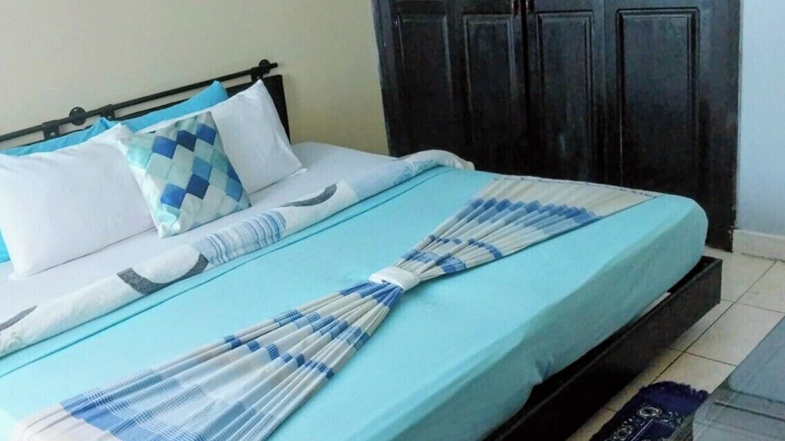 Un lit avec une couvre-lit bleue, des oreillers blancs et un coussin à carreaux.
