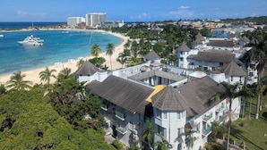 Une station balnéaire dotée de villas en bord de mer, d’un port de plaisance et d’un hôtel situé en arrière-plan.