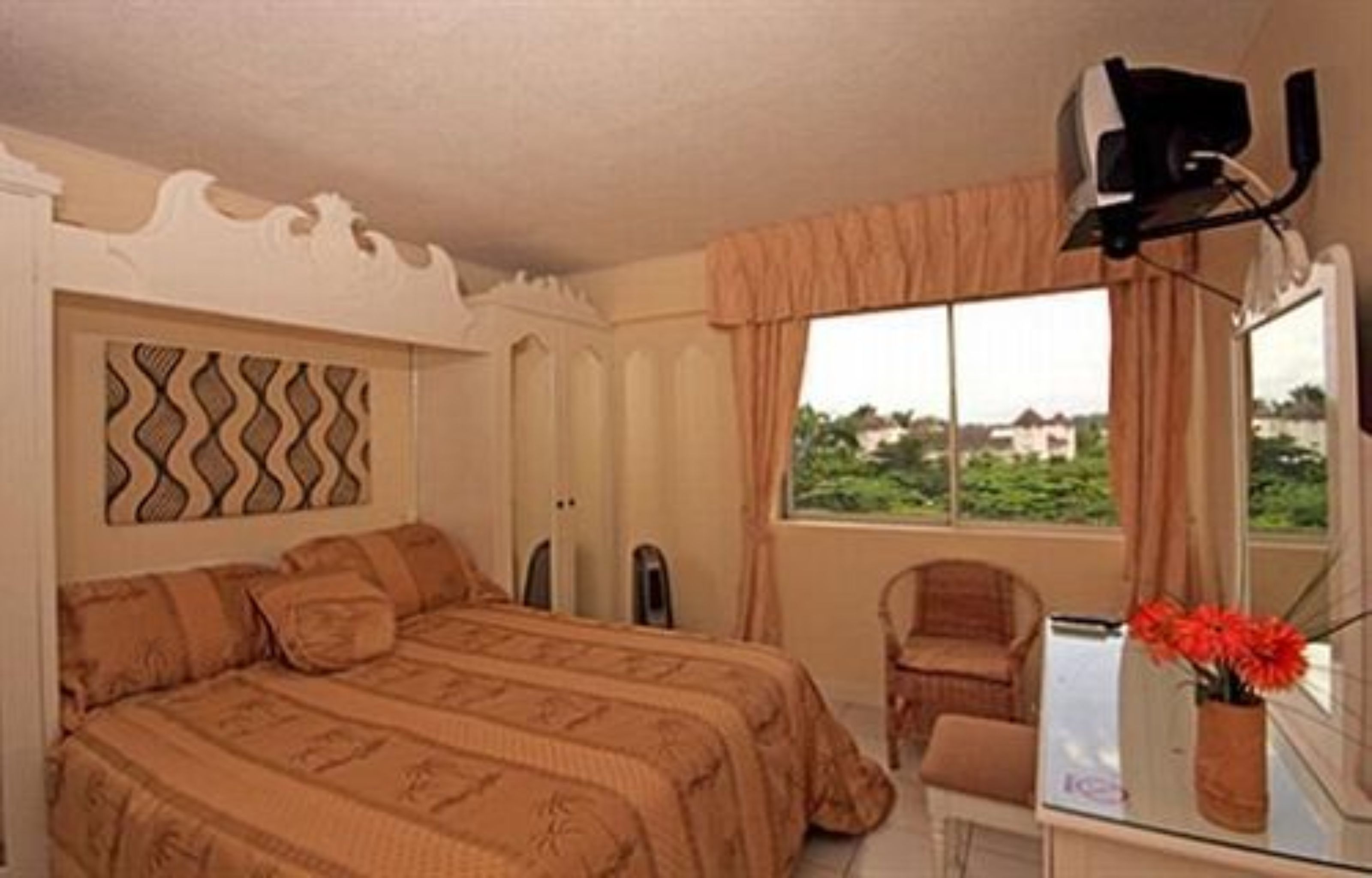A bedroom with a bed, a chair, a desk with a mirror, and a window with a view.