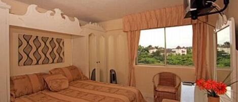 A bedroom with a bed, a chair, a desk with a mirror, and a window with a view.