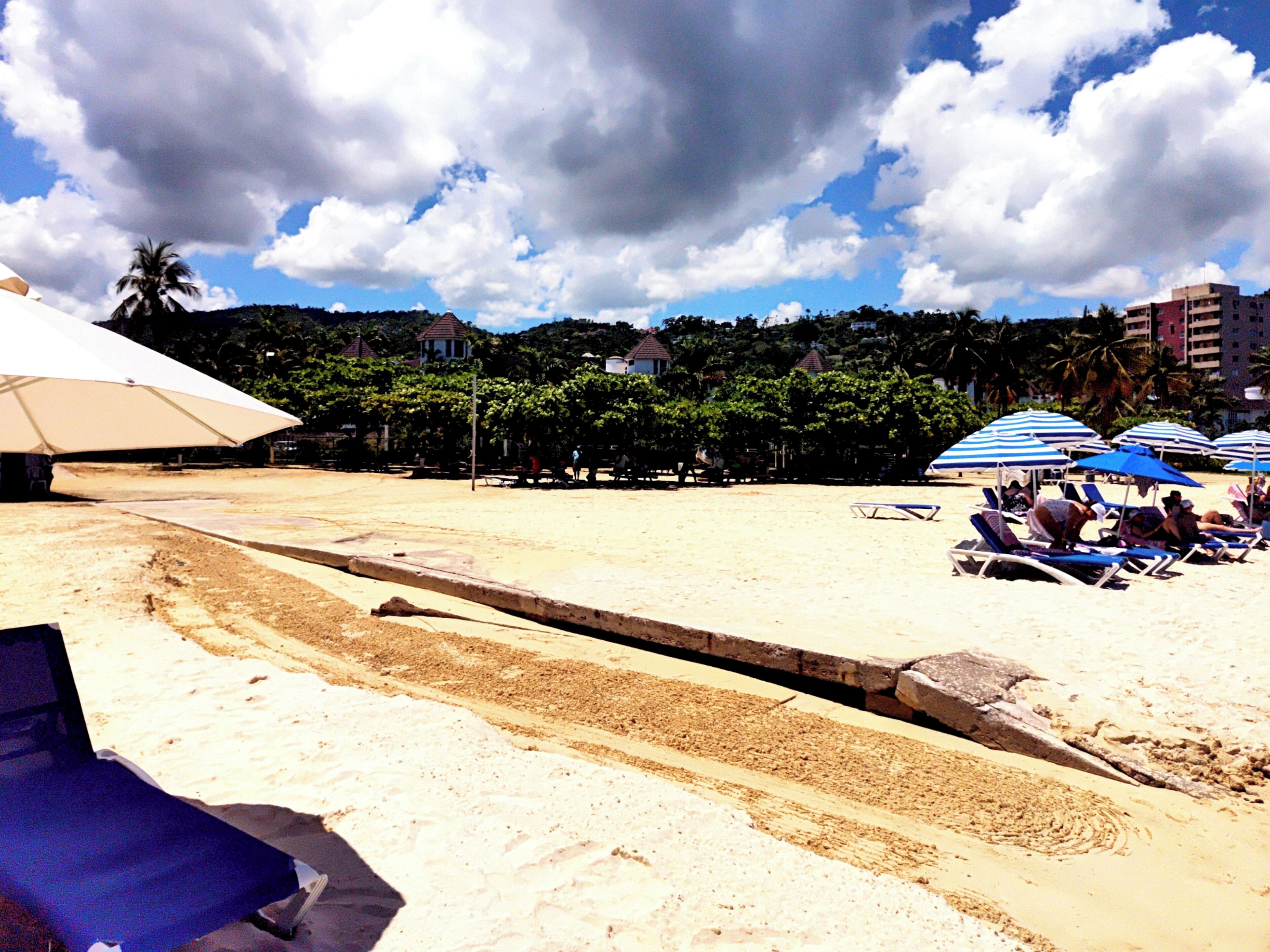 Ein Strand mit Sonnenschirmen, Liegestühlen und einem Sandweg.