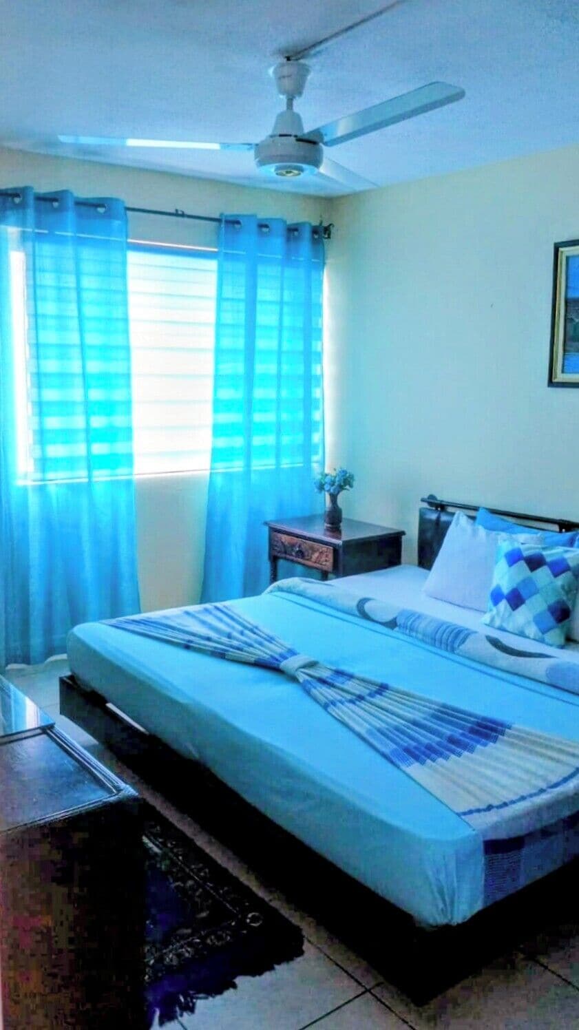 A bedroom with a bed, a nightstand, a ceiling fan, and a window with curtains.