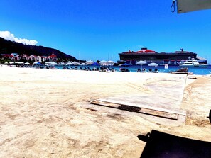 A beach with a large cruise ship docked, umbrellas, and a sandy shore.