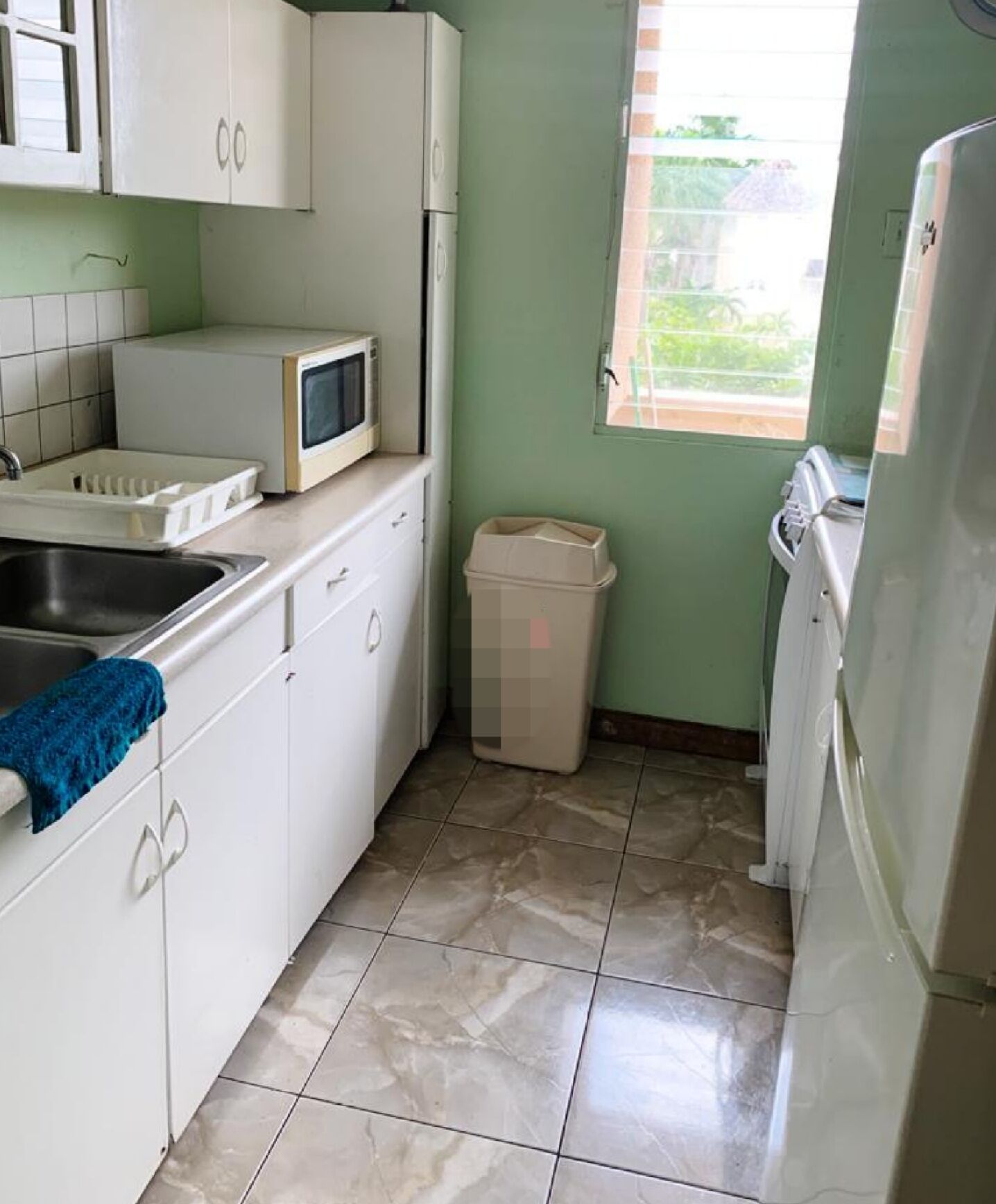 A compact kitchen with white cabinets, a microwave, a sink, and a window.