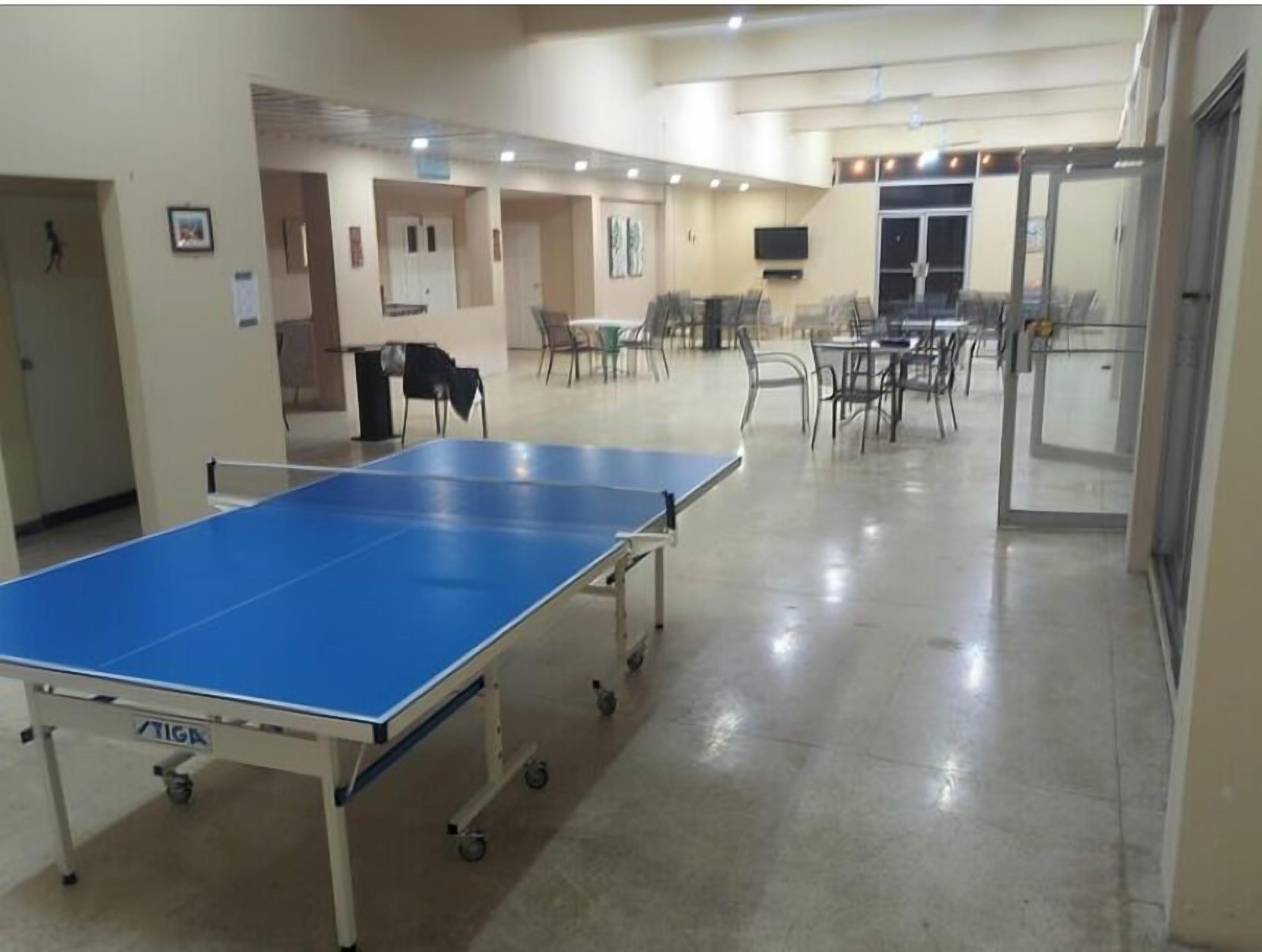 A ping pong table in a room with chairs and tables, a door, and a television on the wall.