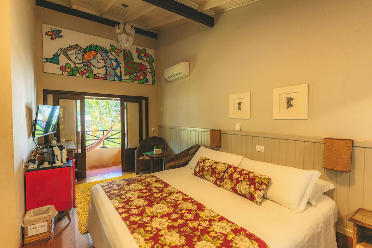 A hotel room with a bed, a desk with a computer, a chair, a window with a view, and a wall with artwork.