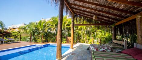 A pool area with a covered seating area, a pool, and surrounding palm trees.