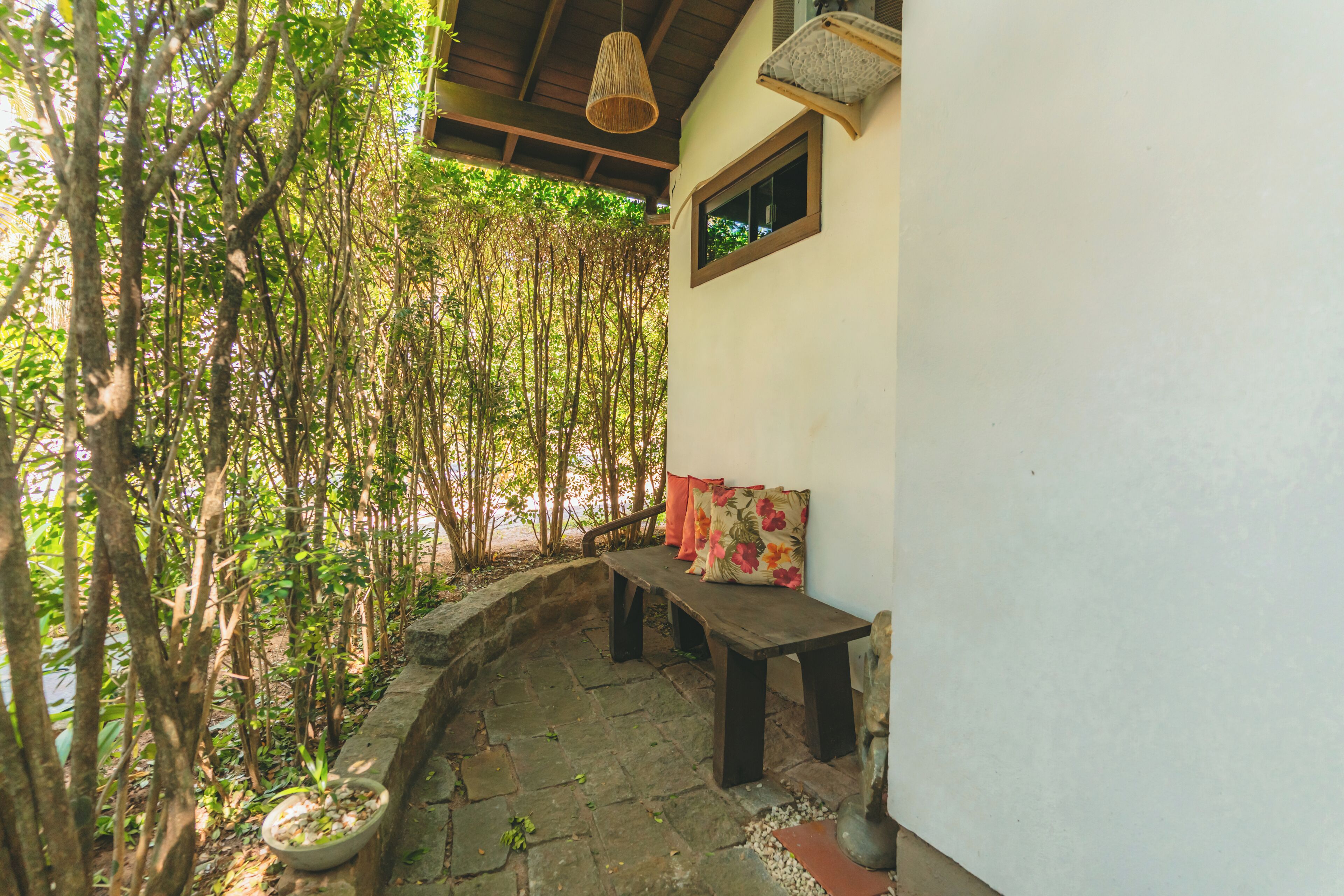 Un banco de piedra bajo una pérgola de madera con una planta en maceta a un lado.