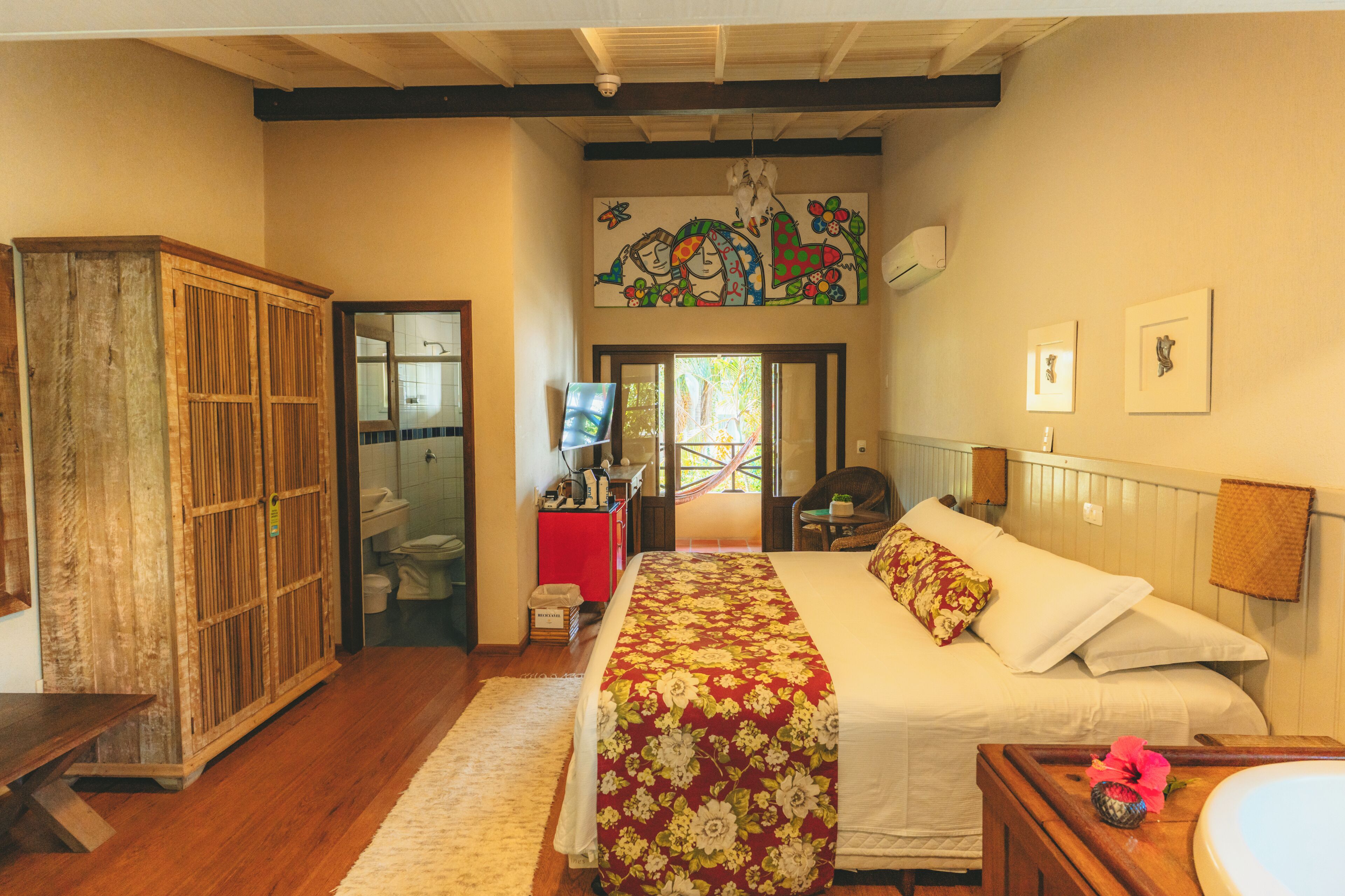 Une chambre à coucher avec un grand lit, une armoire en bois et une salle de bain visible à travers une porte ouverte.