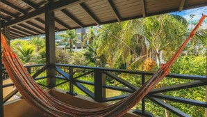 Una hamaca bajo un balcón de madera con vistas a vegetación exuberante y palmeras.