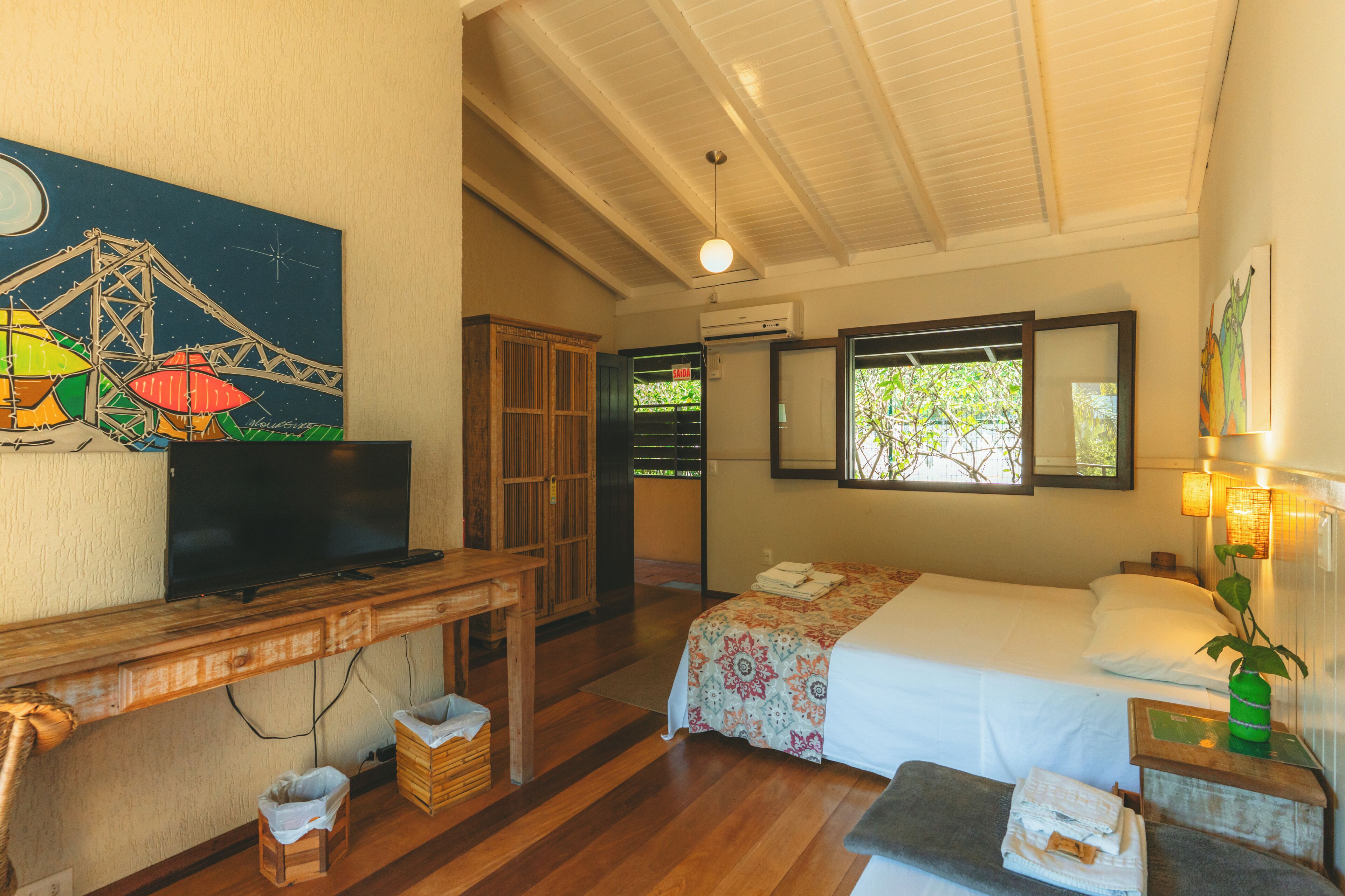 A room with a bed, a desk with a television, a wooden cabinet, and a painting on the wall.