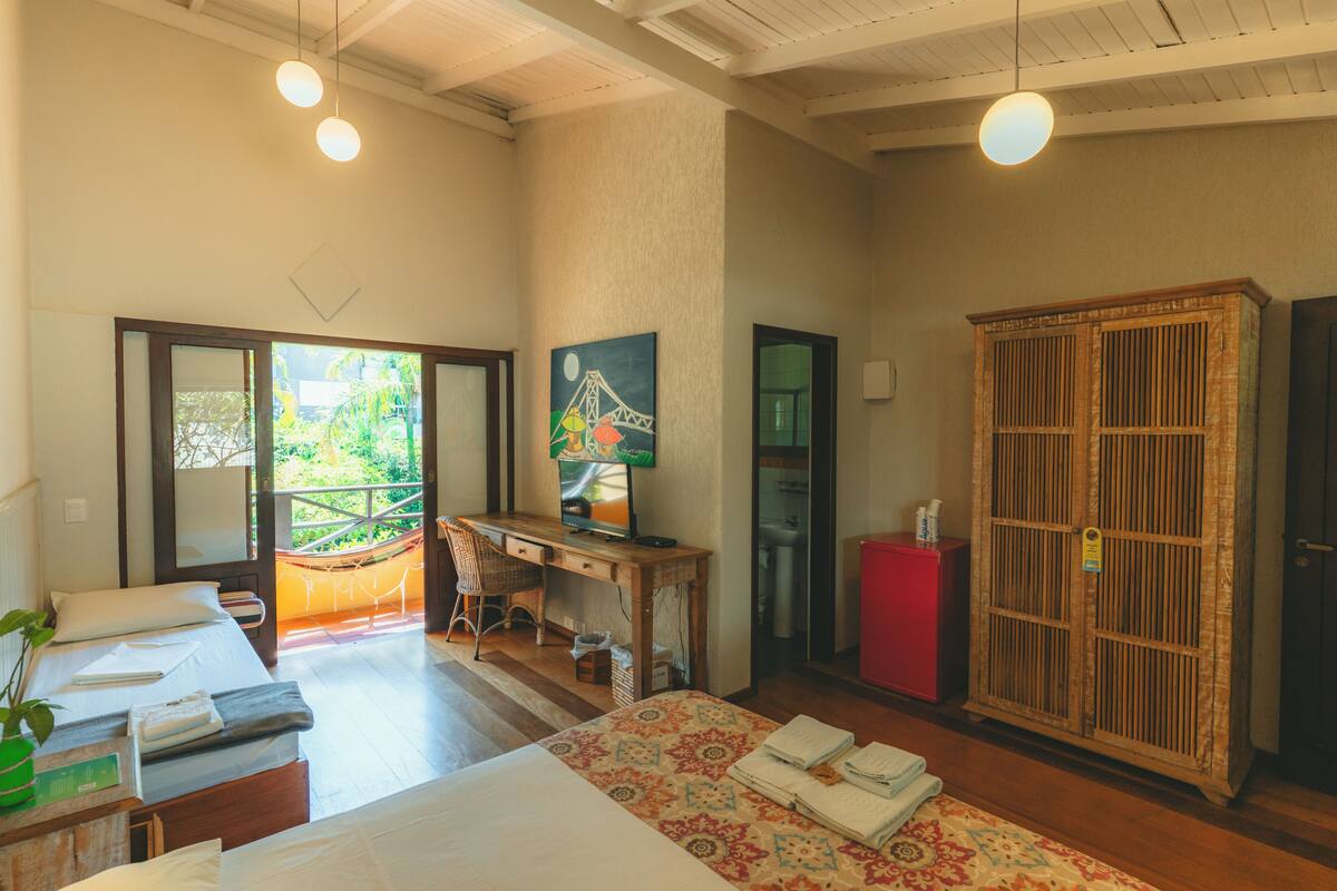A hotel room with a bed, a desk with a computer, a wardrobe, and a view of the outdoors.