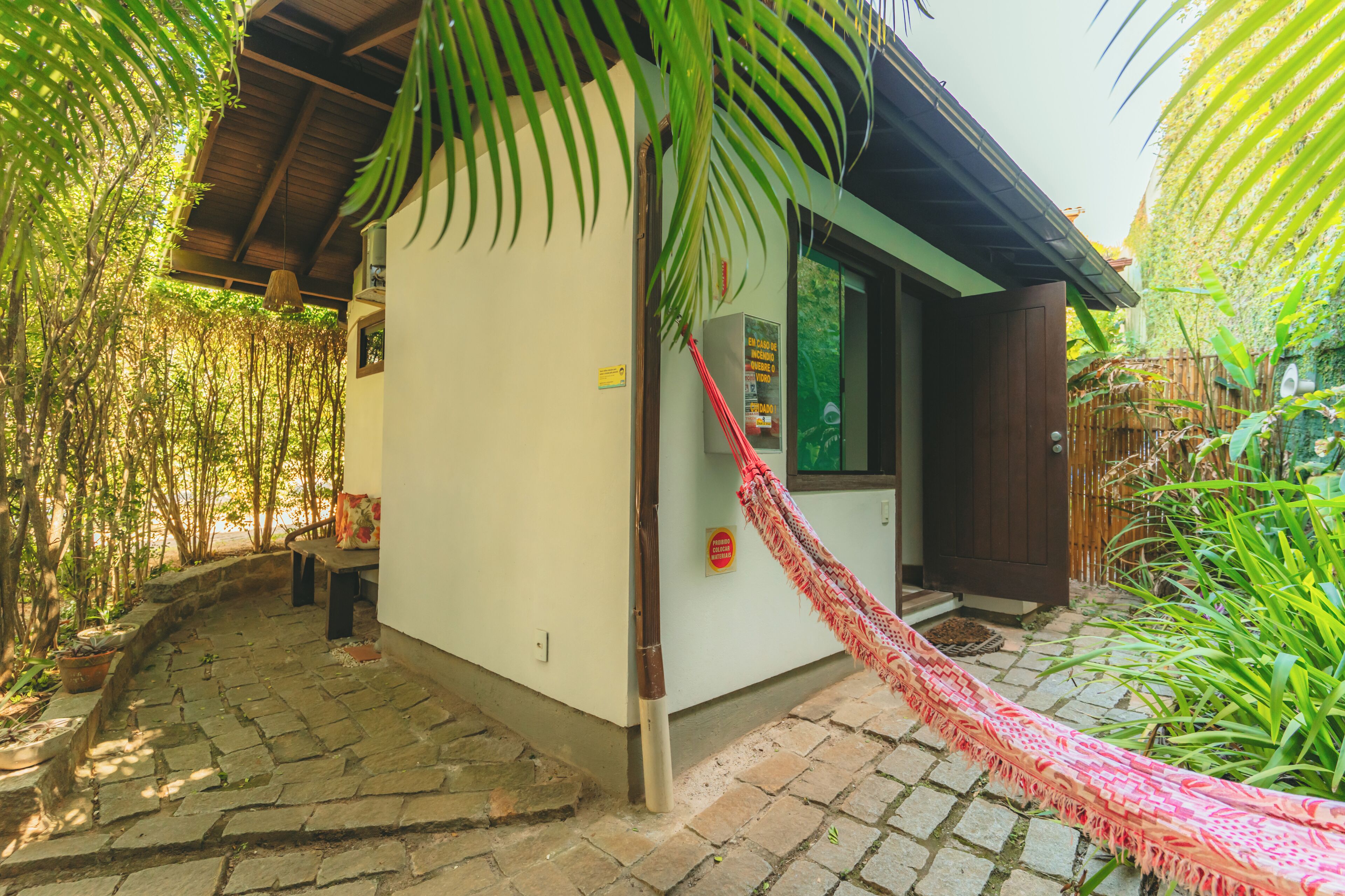 A small building with a white exterior, a wooden door, and a red hammock.