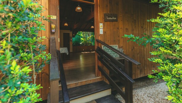 Entrada de un edificio de madera con una escalera que conduce al interior, rodeada de vegetación.