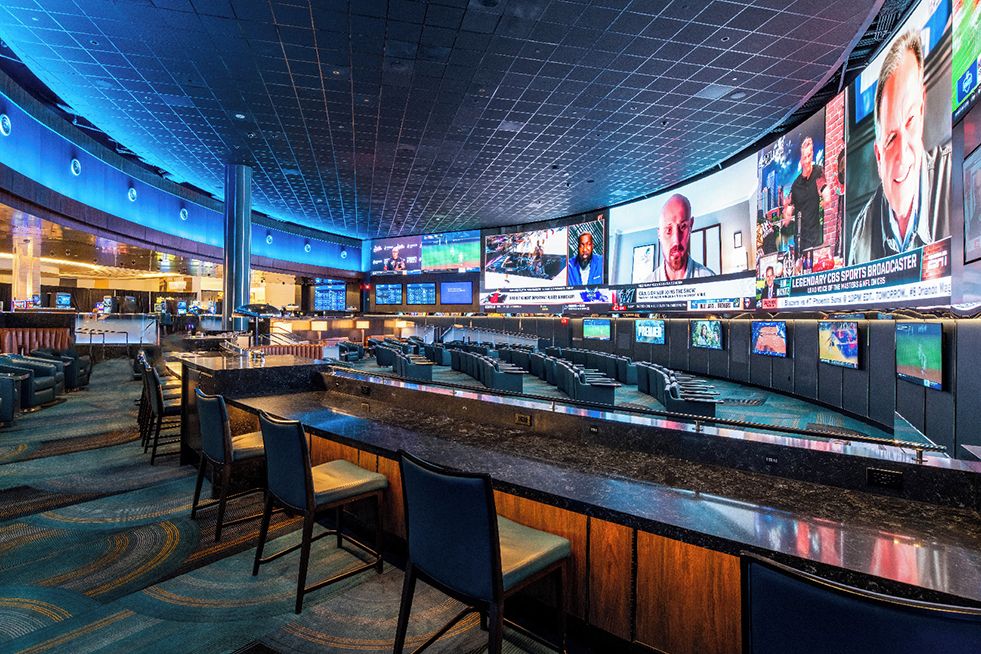 A modern bar area with multiple screens displaying sports content, seating arrangements, and a counter with bar stools.