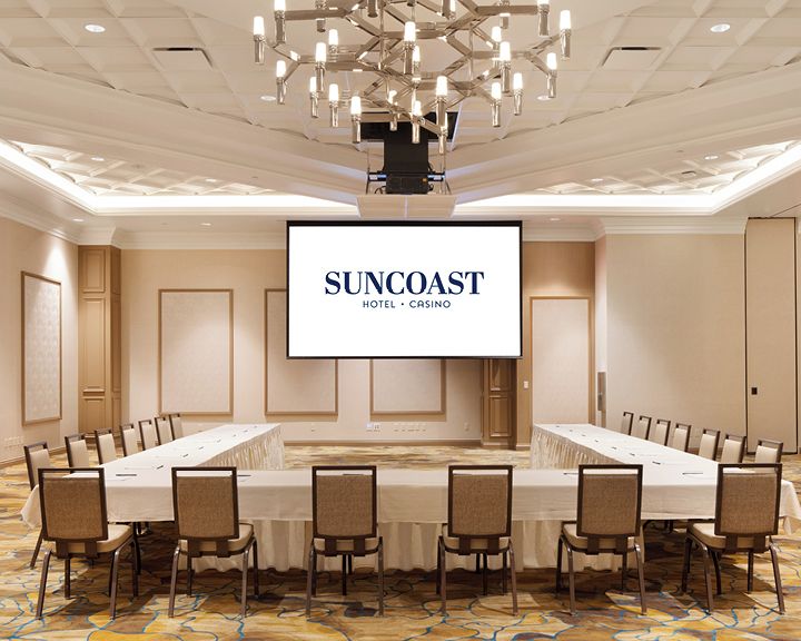 A conference room with a long table, chairs, a screen displaying 'SUNCOST HOTEL - CASINO', and a chandelier.