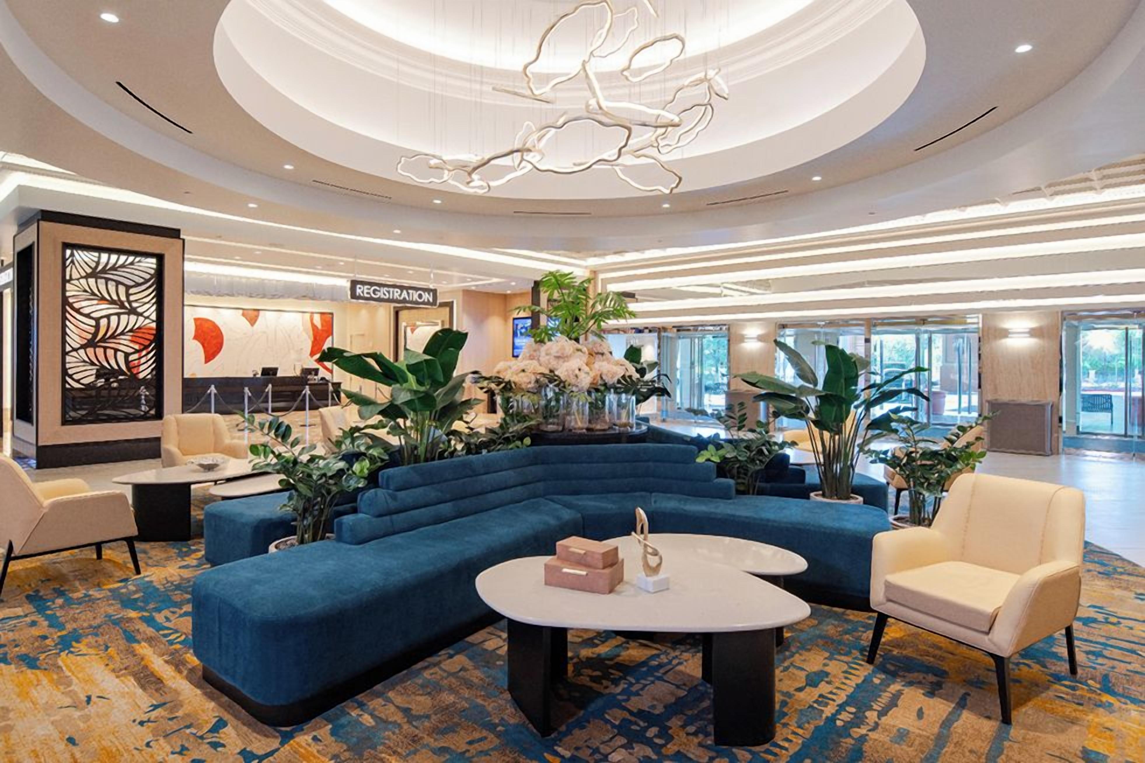 Un hall d’entrée moderne avec un canapé d’angle bleu, un comptoir d’accueil et une grande plante décorative.