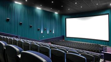 An empty movie theater with rows of seats, a large screen, and teal walls.