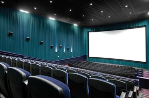 Une salle de cinéma vide, avec des rangées de sièges, un grand écran et des murs de couleur turquoise.