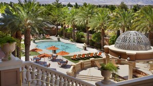 Zona de piscina en un resort, con palmeras, sillas de descanso y una gran estructura en forma de cúpula.