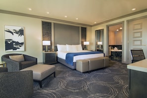 A hotel room with a large bed, two bedside tables with lamps, a seating area with a sofa and armchair, and a bathroom visible through an open door. - Suncoast Hotel and Casino (Las Vegas)