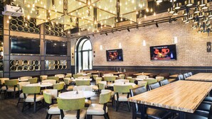 Un restaurante con mesas y sillas redondas, una pared de ladrillo y una pantalla grande mostrando un fuego.
