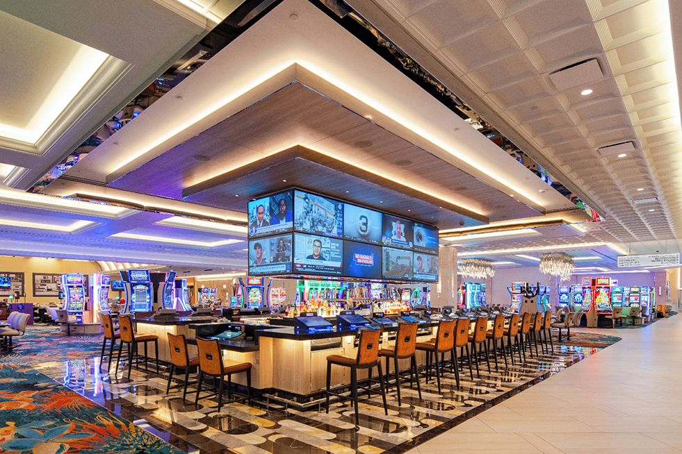 A casino with multiple gaming tables and a large screen displaying various games.