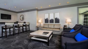 A hotel room with a dining area, a sofa, a coffee table, and a TV.