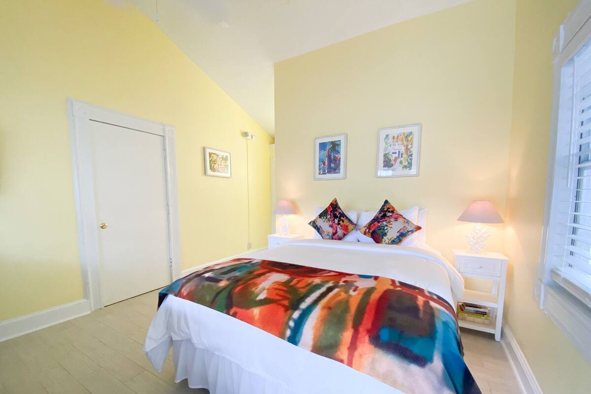 A bedroom with a bed, two bedside tables, a door, and two wall-mounted lamps.