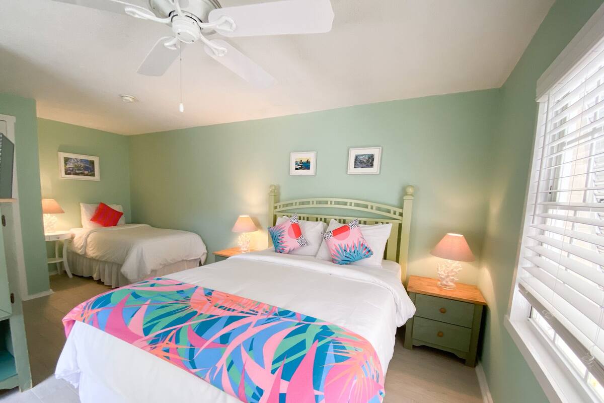 A bedroom with a bed, two bedside tables, a ceiling fan, and a window with blinds.