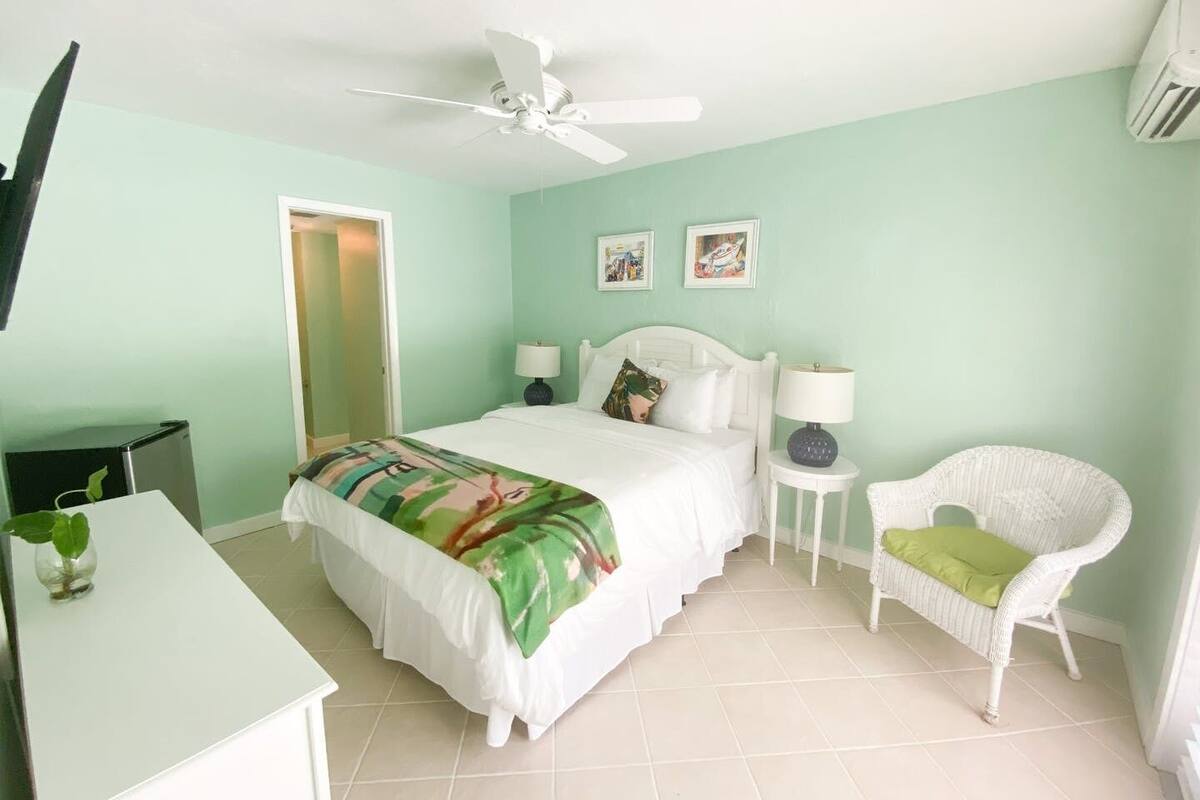 A bedroom with a bed, two bedside tables, a chair, a ceiling fan, and a television.