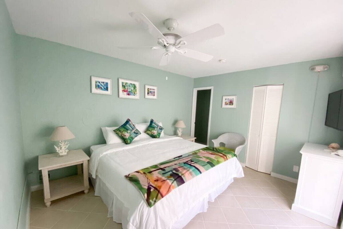 A bedroom with a bed, a nightstand, a chair, a desk, and a ceiling fan.