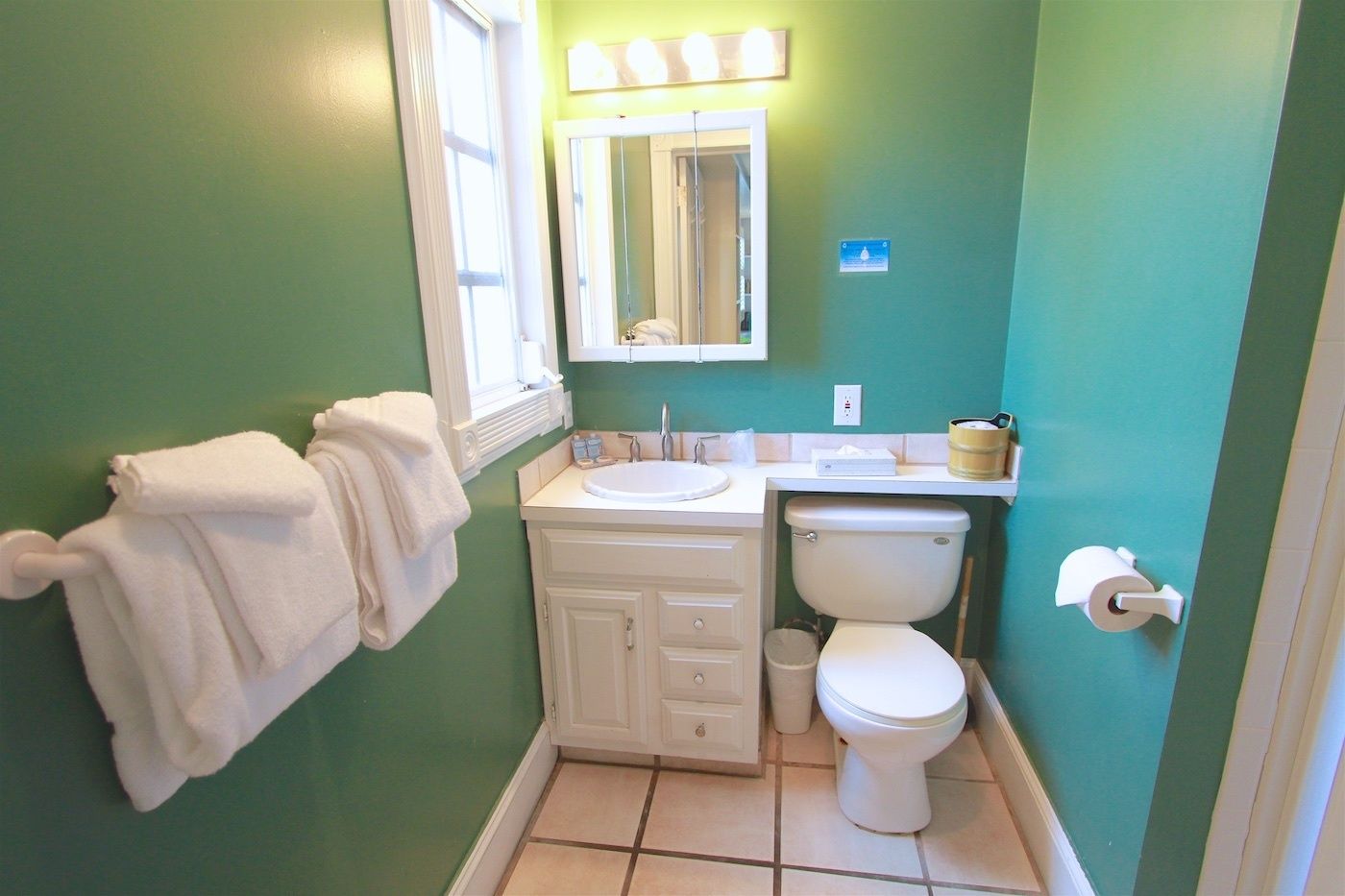 A bathroom with a green wall, white fixtures, a sink, a toilet, and a towel rack.