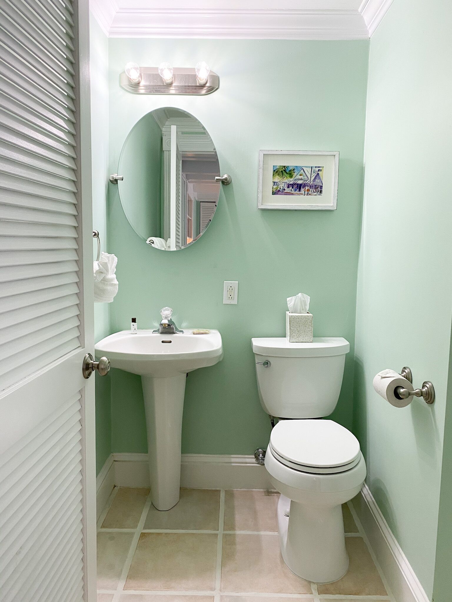 A bathroom with a sink, toilet, mirror, and a framed picture on the wall.